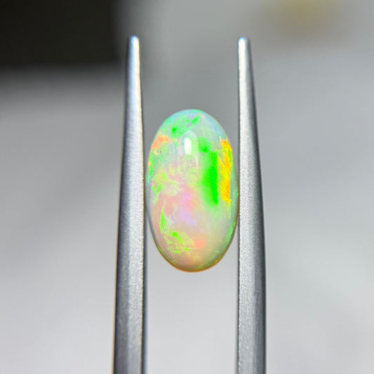 Opal gemstone held between tweezers against a blurred background